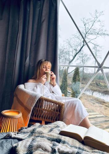 a woman sitting in a chair drinking a cup of coffee at Heaven Reset Spa Luksusowy Glamping Jacuzzi w Naturze Blisko Warszawy in Korczew