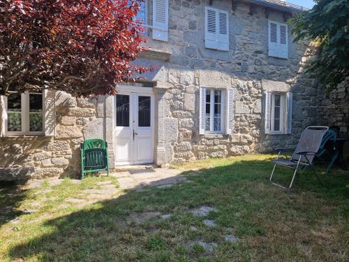 a stone house with a white door and a chair at Maison paysanne, proche Aubrac in Huparlac