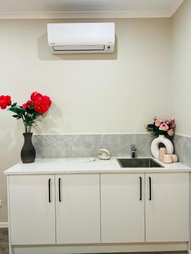 a white kitchen with a sink and red roses at Modern One Bedroom Unit with Private Entrance Near Hunua Falls in Hunua