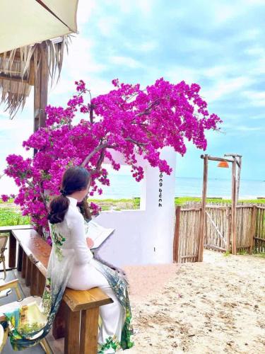 a woman sitting on a picnic table with a bougainvillea at Hoàng Nga 2 Homestay in Phan Thiet