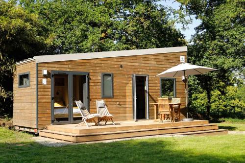 a small wooden cabin with chairs and an umbrella at FORET TOTEM - Hébergements nature et bien-être en pleine forêt in Persquen