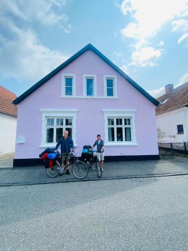 Dos personas en bicicleta frente a una casa morada en Stub Inn Guesthouse, en Stubbekøbing