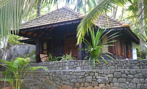 a small house with a stone wall in front of it at Niraamaya Wellness Retreats, Surya Samudra, Kovalam in Kovalam