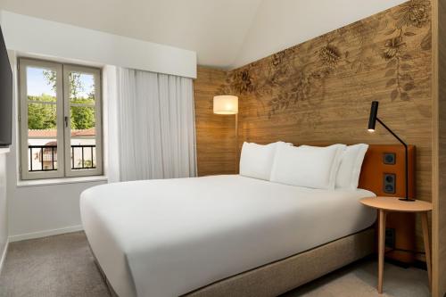 a bedroom with a large white bed and a window at Dolce by Wyndham Versailles - Domaine du Montcel in Jouy-en-Josas
