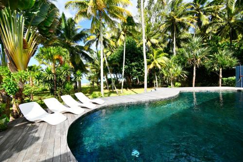 a swimming pool with white chairs and palm trees at Villa Philibert in Riambel