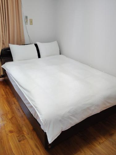 a white bed with two pillows on top of it at アンガマの宿 in Naha