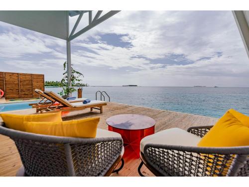 a patio with chairs and a table and the ocean at Oaga Art Resort Maldives - Greatest All Inclusive Plan with Free Speedboat Round-trip in North Male Atoll