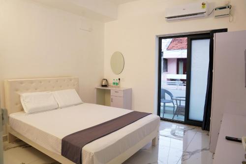 a white bedroom with a bed and a balcony at La Maison Du Bonheur in Pondicherry