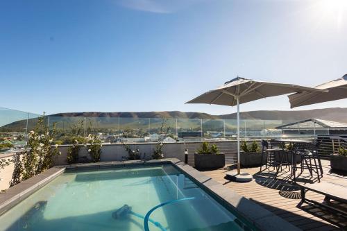 a swimming pool with an umbrella and tables and chairs at Ocean-View Studio Apartment, Hermanus Waterfront - Apt 8 in Hermanus