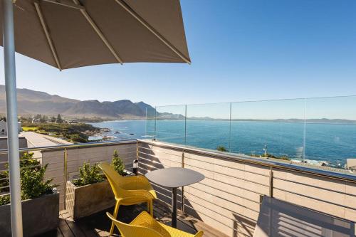 a balcony with chairs and a table and an umbrella at Ocean-View Studio Apartment, Hermanus Waterfront - Apt 8 in Hermanus