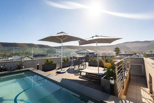 a balcony with a swimming pool and umbrellas at Ocean-View Studio Apartment, Hermanus Waterfront - Apt 8 in Hermanus