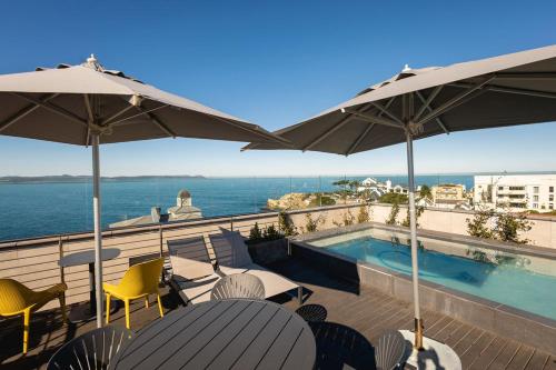 a balcony with a swimming pool and chairs and umbrellas at Ocean-View Studio Apartment, Hermanus Waterfront - Apt 8 in Hermanus