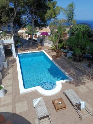 a large swimming pool with chairs and the ocean at Villa les Pins in Jávea