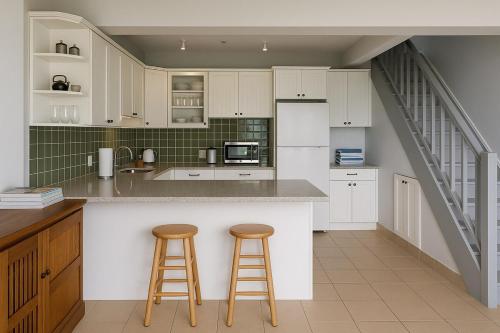 a kitchen with white cabinets and two bar stools at BluEdge Villa VIP Resort Access in Tortola Island