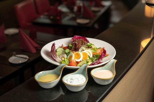 a salad in a white bowl on a table with spoons at Ramada by Wyndham Essen in Essen