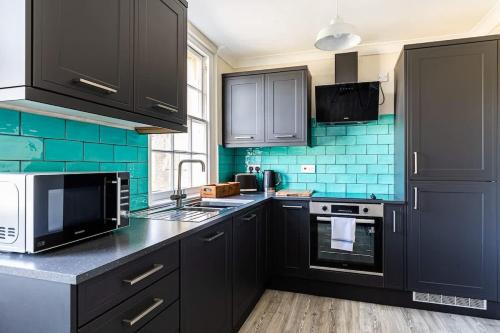 a kitchen with black cabinets and blue tile at Margarets Buildings Bath City Centre in Bath