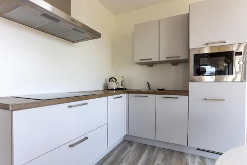 Una cocina blanca con gabinetes blancos y un microondas. en Uithaven 10B Kamperland, with harbour views, en Kamperland