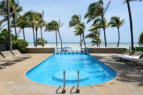 a swimming pool next to the beach with palm trees at Departamento Mayan Lakes T9 - Albercas, club de playa, tenis, pádel y más in Acapulco