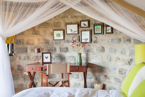 a bedroom with a desk and a stone wall at Ololo Safari Lodge & Farm in Nairobi
