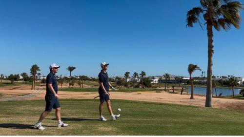 two men walking on a golf course near a palm tree at Pickalbatros Golf Luxury Suites - All Inclusive in Sharm El Sheikh
