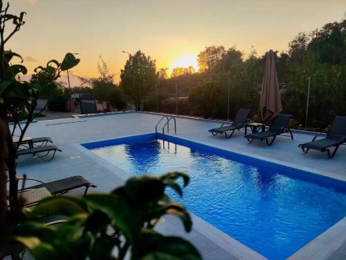 a swimming pool with chairs and a sunset in the background at Tarmaros - Families & Groups in Sissi