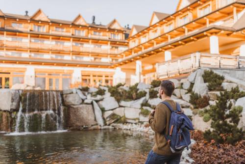 a man with a backpack standing in front of a building at Hotel Bania Thermal & Ski in Białka Tatrzanska