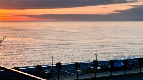 a view of the ocean at sunset with palm trees at Sea Romantic Apartment in Gonio