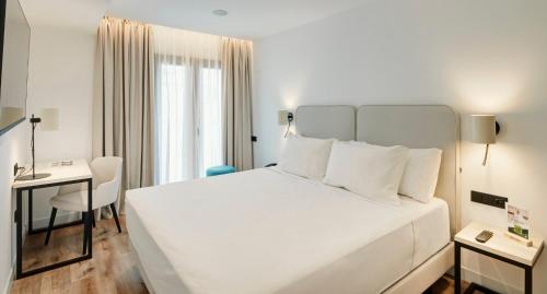 a bedroom with a large white bed and a desk at Sercotel Cruz Del Mar in Chipiona