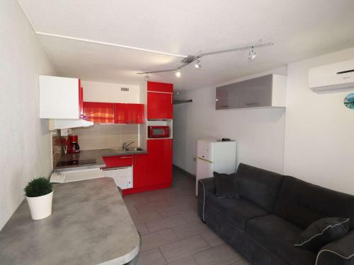 un salon avec un canapé et une cuisine avec des armoires rouges dans l'établissement Studio climatisé proche mer avec terrasse, park privé et équipements modernes - FR-1-307-198, au Grau-du-Roi