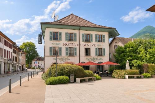 ファヴェルジュにあるLogis Hôtel de Genève et Restaurant , Faverges-Seythenexの通りに面したテーブルとパラソルのあるホテルの建物