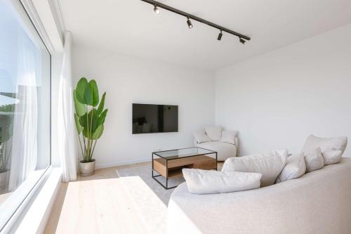 a white living room with a white couch and a tv at Huswell - New Beach Apartment in De Haan in De Haan