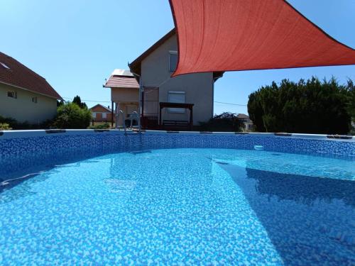 a swimming pool with a red umbrella next to a house at Gyöngy-ház Balaton, önálló nyaraló in Szőlősgyörök