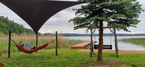 a person laying in a hammock next to a lake at Agroturystyka Katarzyna Tarasiewicz in Stary Folwark