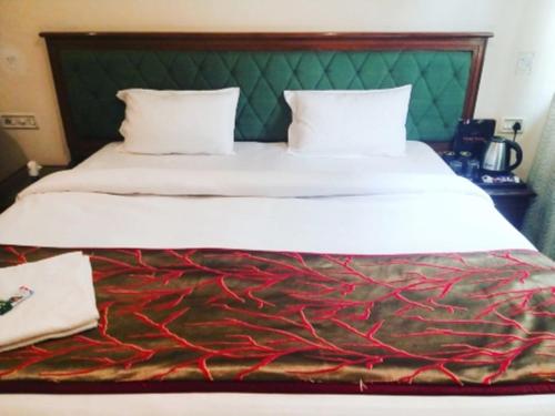 a large bed with white sheets and a green headboard at Hotel Saket In Prayagraj in Prayagraj