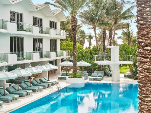 a hotel pool with chairs and umbrellas and palm trees at The Shelborne by Proper, a Member of Design Hotels in Miami Beach