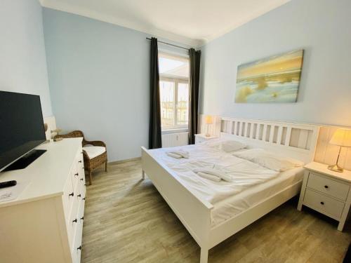 ein weißes Schlafzimmer mit einem Bett und einem Fernseher in der Unterkunft Berringer, Knurrhahn, direkt an der Promenade in Warnemünde