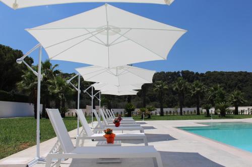 a row of white lounge chairs with umbrellas next to a pool at Dani's residence in Supersano