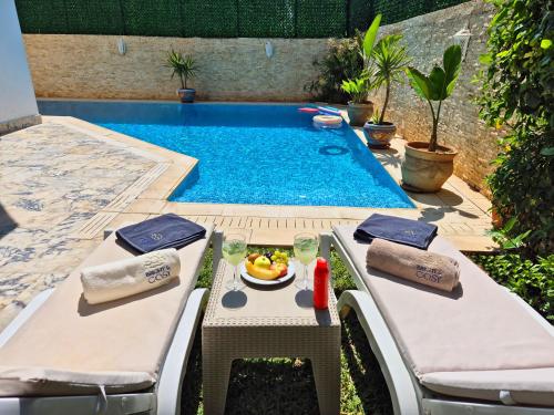 a pool with two chairs and a table with a bowl of fruit at L'Orchidée - Suites de Luxe avec Piscine Chauffée et Vue sur le Lac de Tunis in Tunis