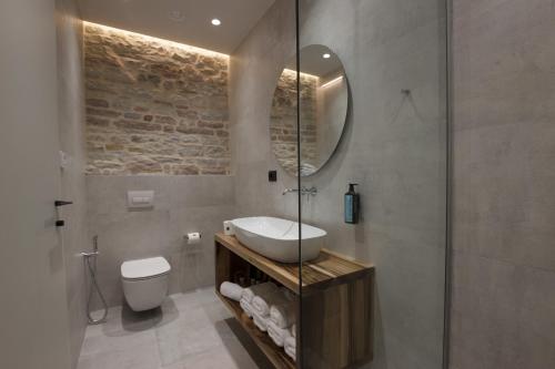 a bathroom with a sink and a toilet and a mirror at Stitch&Stone Suites in Gjirokastër