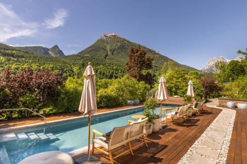 a pool with chairs and umbrellas with mountains in the background at Berghotel Rehlegg in Ramsau