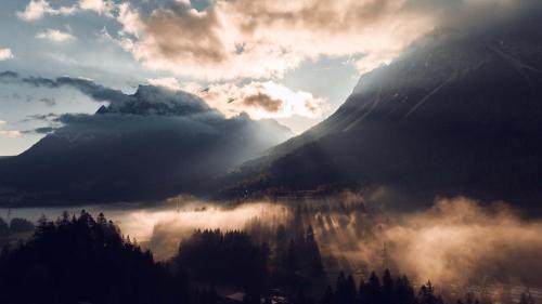 a mountain shrouded in clouds with the sun shining on it at Silberleithen Estate in Biberwier