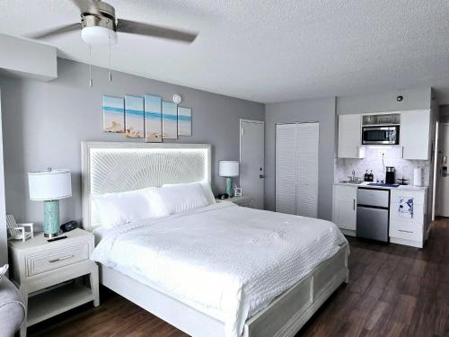 a bedroom with a white bed and a kitchen at Oceanview 2 Studios adjoining w/pool, kitchenettes in Daytona Beach