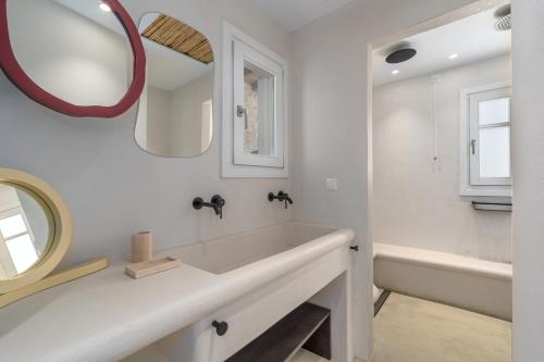 a white bathroom with a tub and a mirror at Petradi Studios & Villa in Aegiali