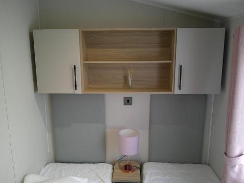 a room with two beds and a cabinet and a lamp at Kings Ashington 6 Berth Central Heated Enclosed Veranda in Chapel Saint Leonards