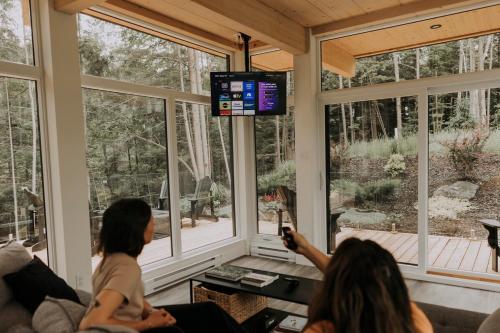a group of people sitting in a living room watching a television at Scenic Bright - Sauna - Fire - 20 min Tremblant in La Conception