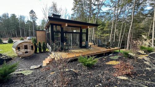 a tiny house in the woods with a wooden deck at Scenic Bright - Sauna - Fire - 20 min Tremblant in La Conception