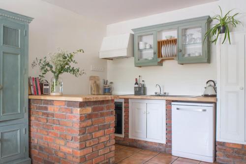 a kitchen with white cabinets and a brick wall at Courtyard Cottages in Tralee