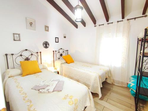 two beds in a room with white walls and yellow pillows at Casa Carámbila in Cómpeta