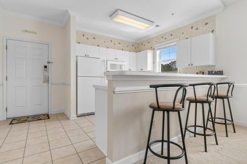 a kitchen with white cabinets and bar stools at Stylish Barefoot Golf Condo with Pool Access in North Myrtle Beach