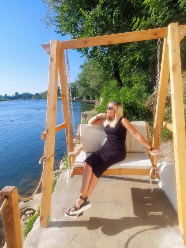 a woman sitting on a swing next to the water at Vikendica Drinski mir in Loznica